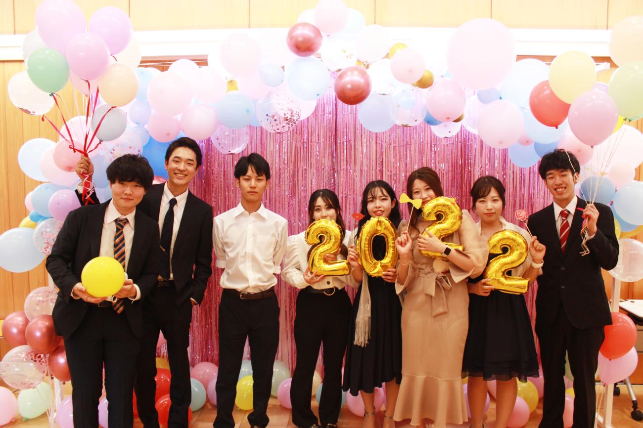 22祭フォトスポットで男性4名と女性4名が数字のバルーンや風船を持って笑顔で記念撮影を行っている写真