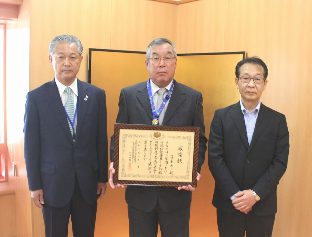 男性3人が横一列に並び、感謝状を持っている佐々木吉一さん(中央)と一緒に記念撮影をしている写真