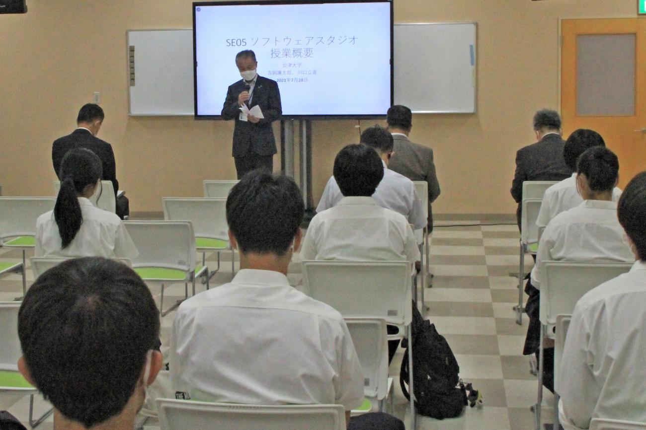 前方に設置されたモニターの前で挨拶をする町長と、椅子に座って聞いている参加者達を後方から写した写真