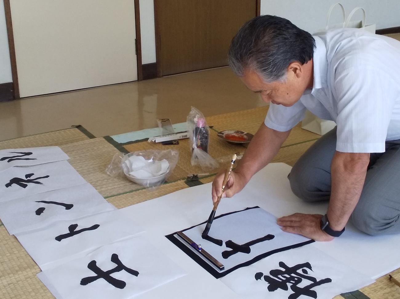 畳が敷かれた部屋で正座をし、習字をしている町長の写真