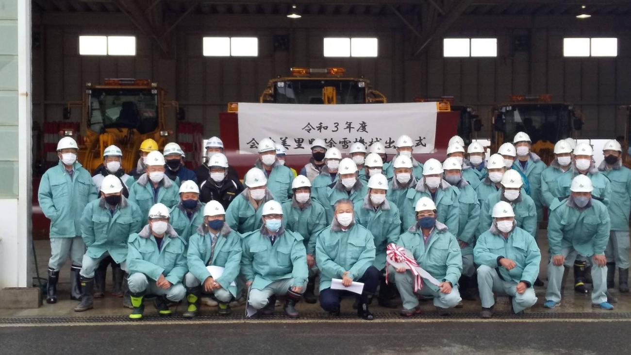除雪機械の前で、ヘルメットを被り作業服を着た除雪機械オペレーターの方々と記念撮影をしている写真