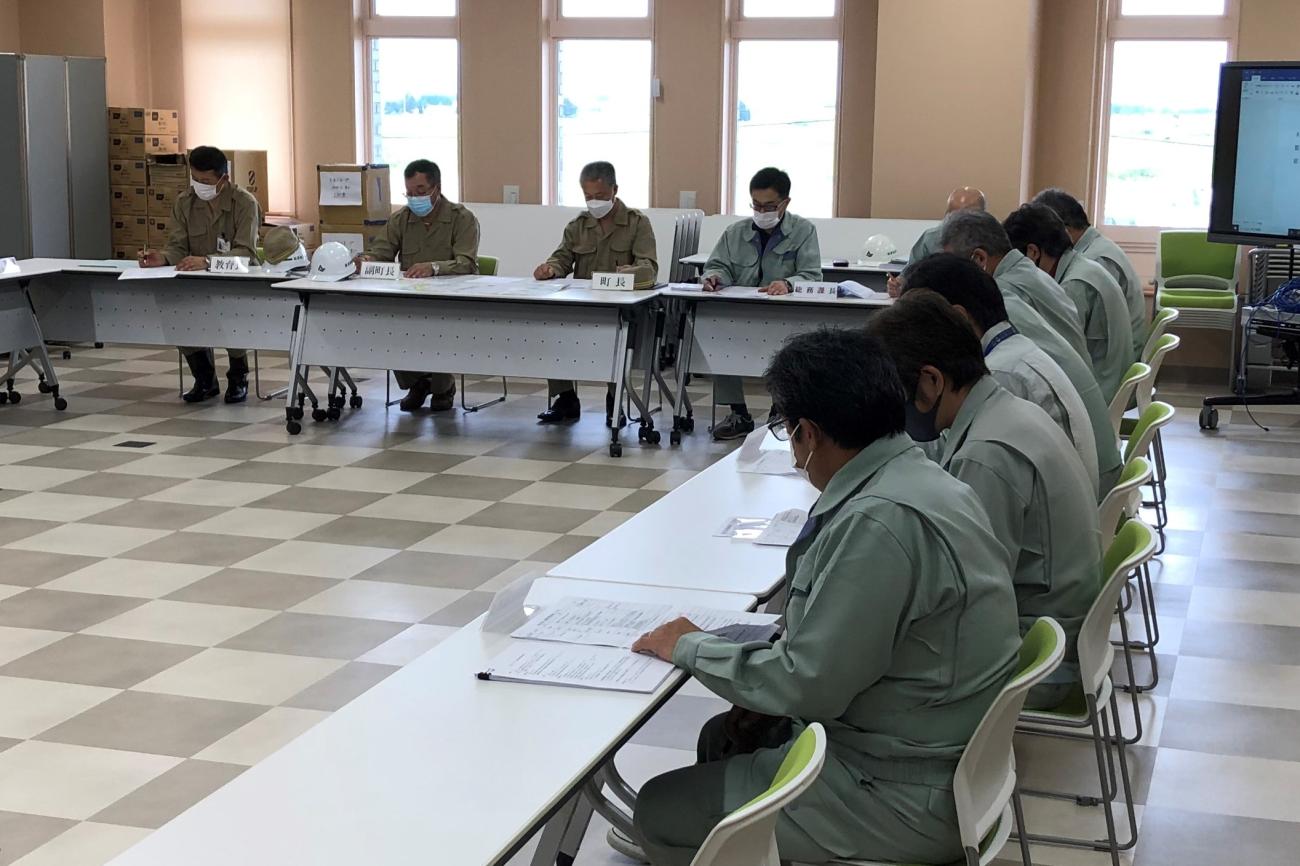 コの字型に設置された長机と椅子に座り、作業服を着た町職員の方々が資料を見ながら確認している写真