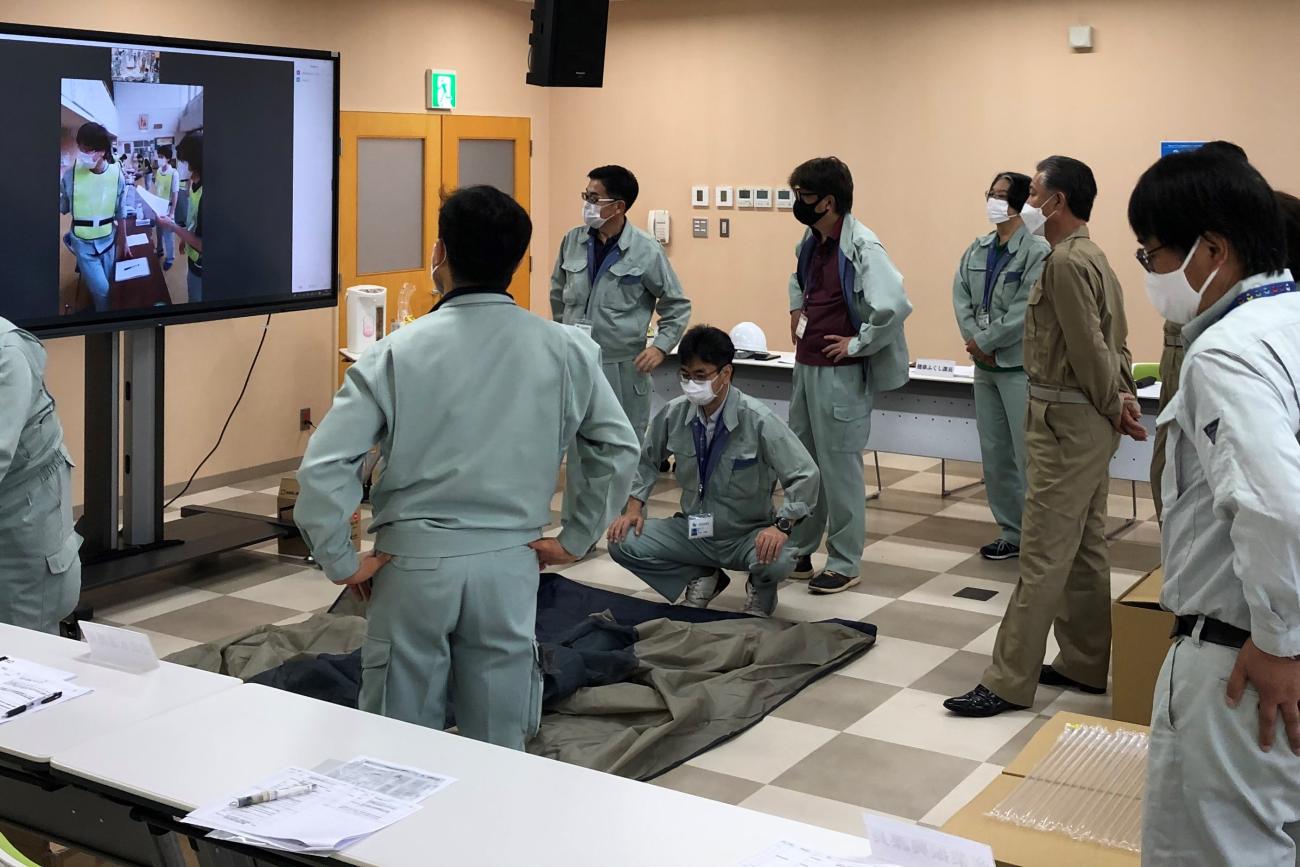 町職員の方々がモニター前に集まり、敷物を床に敷いて映し出された映像を見ながら災害時の対応を確認している写真