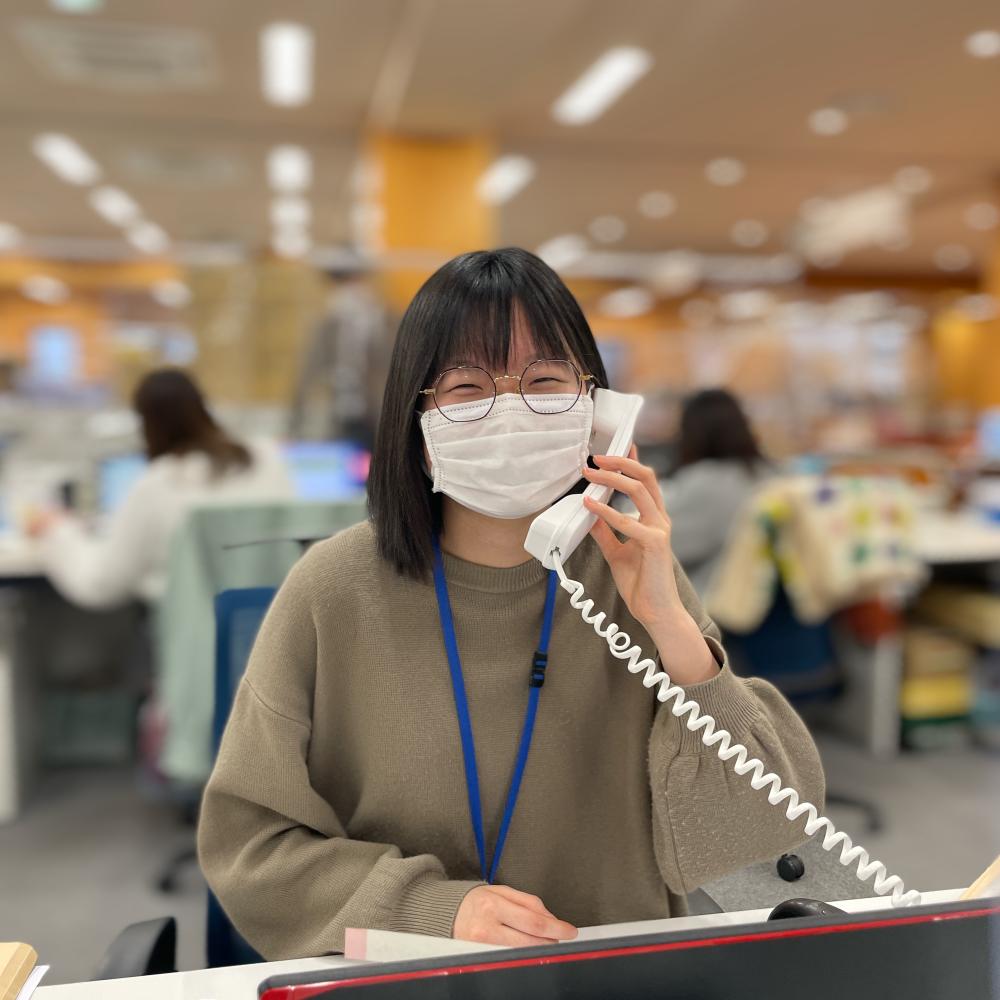 眼鏡をかけた松本奈緒さんが笑顔で電話応対している様子の写真