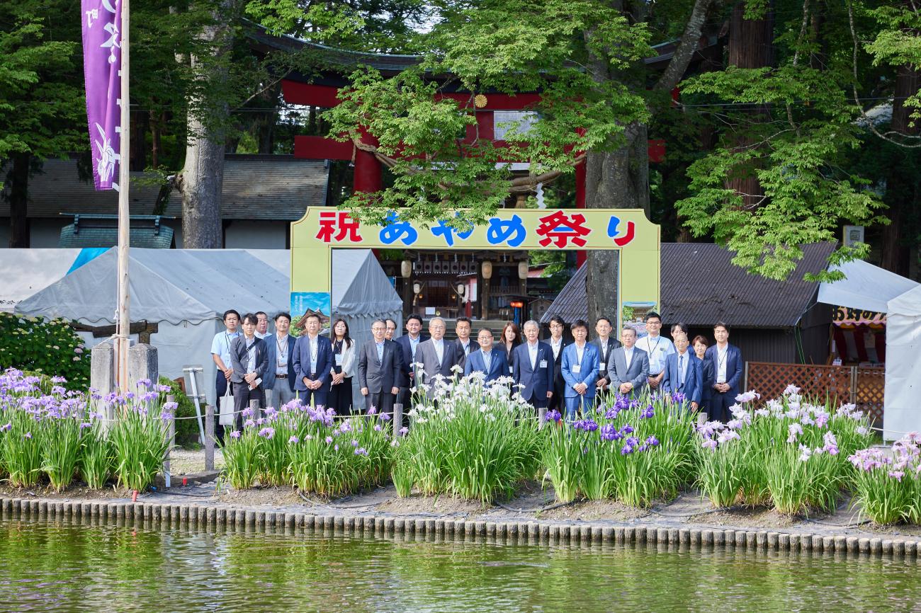 水辺に咲くあやめを前に、「あやめサミット」に参加された方々と記念撮影をしている写真