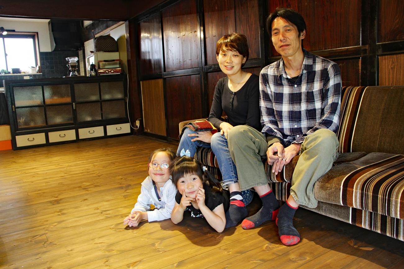 リビングに置かれたソファーに座る岩波さんご夫婦と足元で寝転んでいる2名の子どもの写真