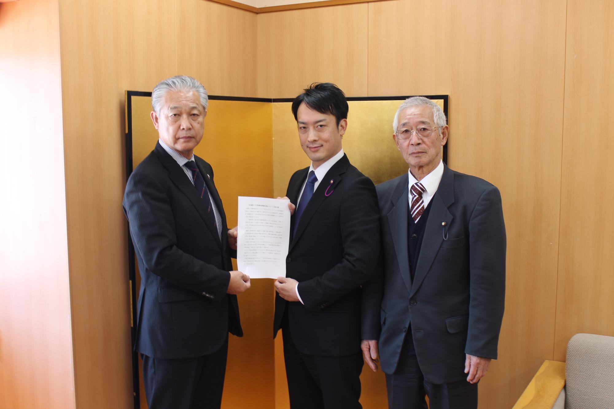 スーツを着た5人が横一列に並び、杉山町長と村松委員長、櫻井委員長が一緒に提言書を持っている写真