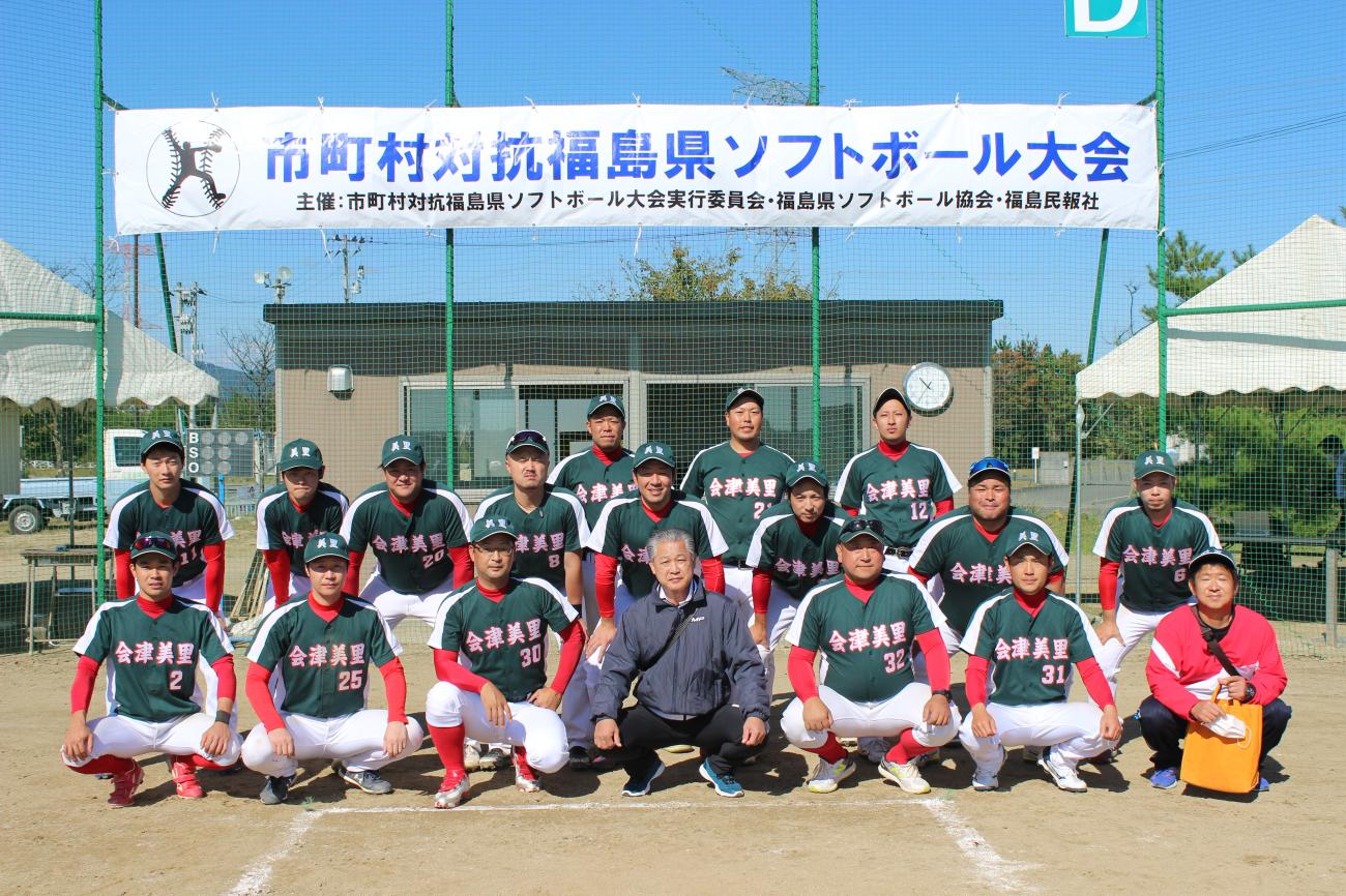 市町村対抗福島県ソフトボール大会と書かれた幕の下に並んで記念撮影をしている選手達の写真