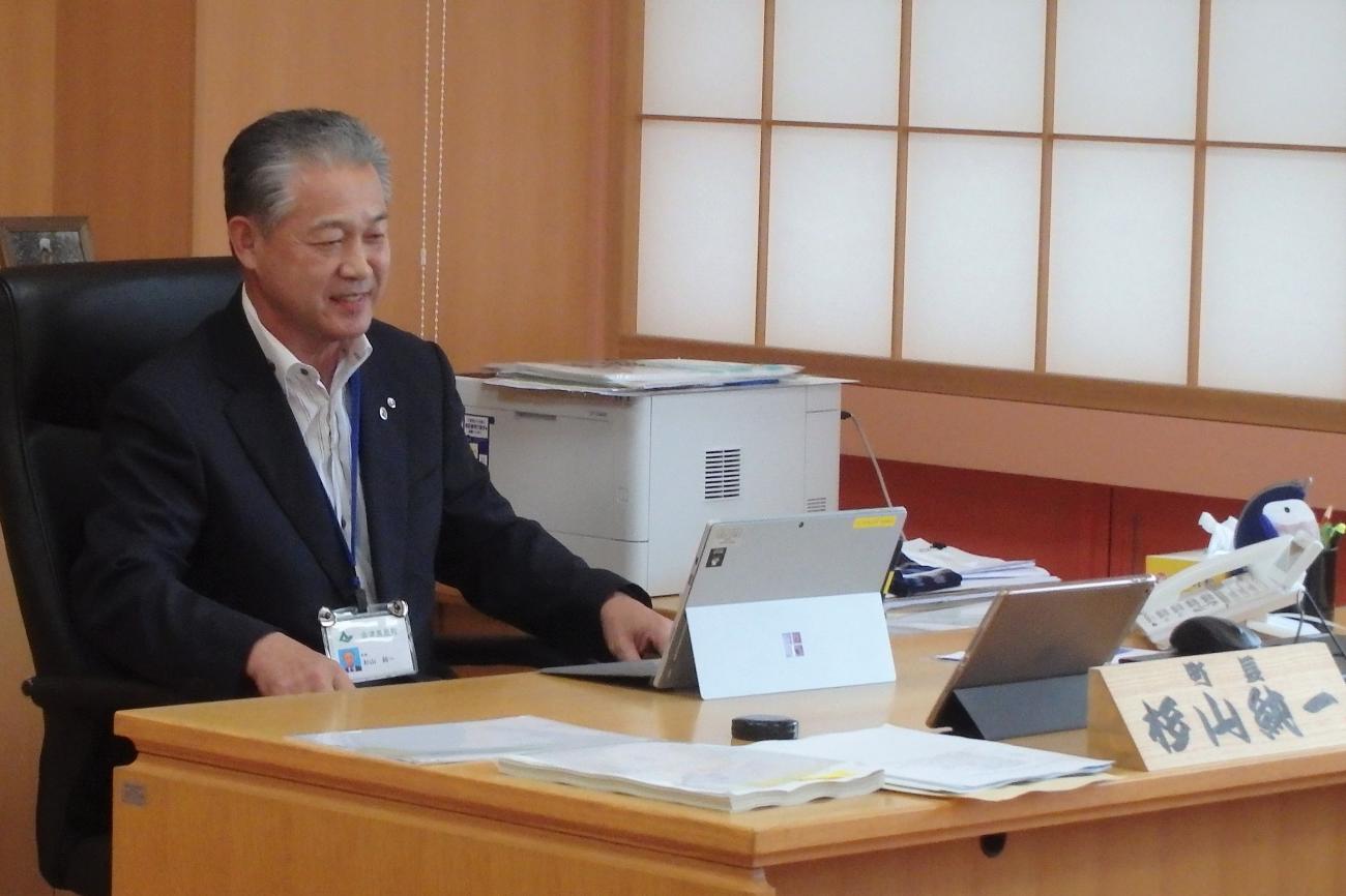 町長室の席に座り、机にパソコンを置いて「オンライン町村役場見学ツアー」に参加している町長の写真