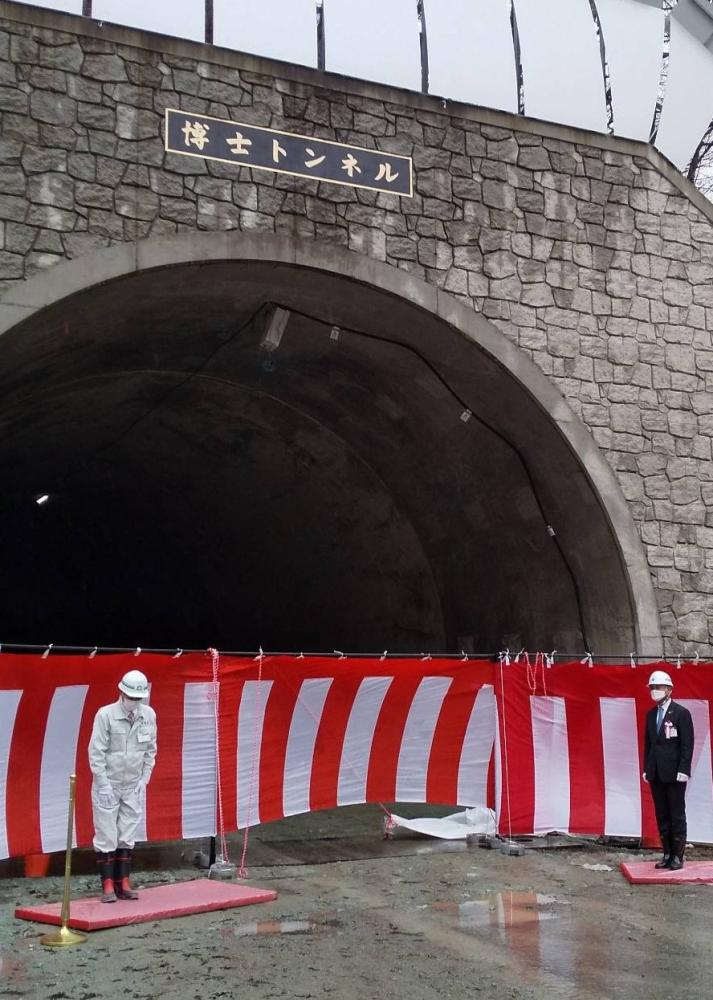 博士トンネルの入り口で行われた除幕式で関係者の人が頭をさげている写真