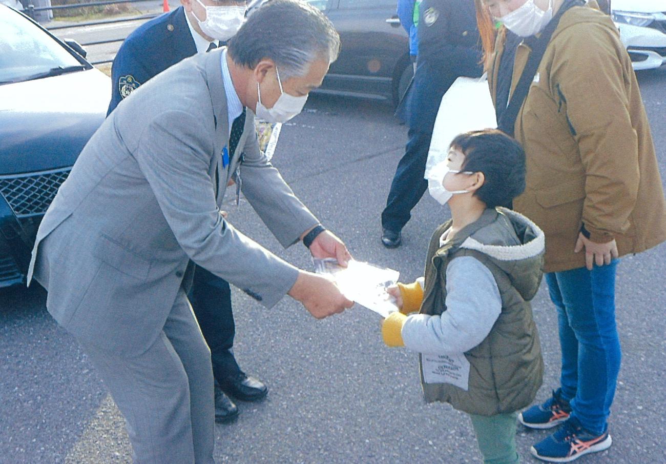 町長が男の子に手渡しでパンフレットを渡し、話しかけている写真