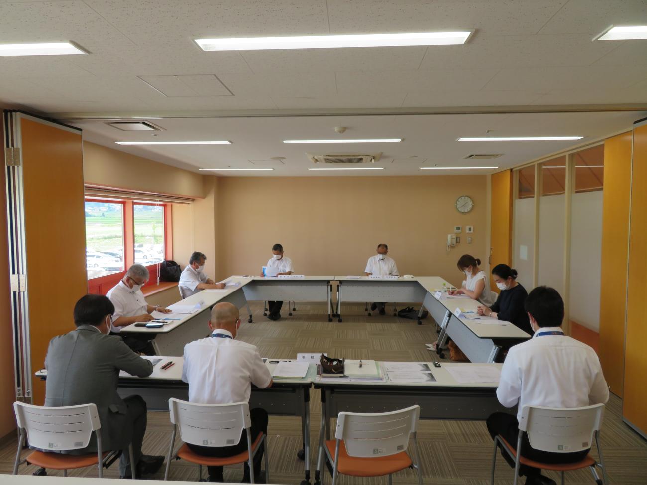 ロ型に机が設置され検討会の参加者の方々が席に着き、資料に目を通している検討会の様子全体を写した写真