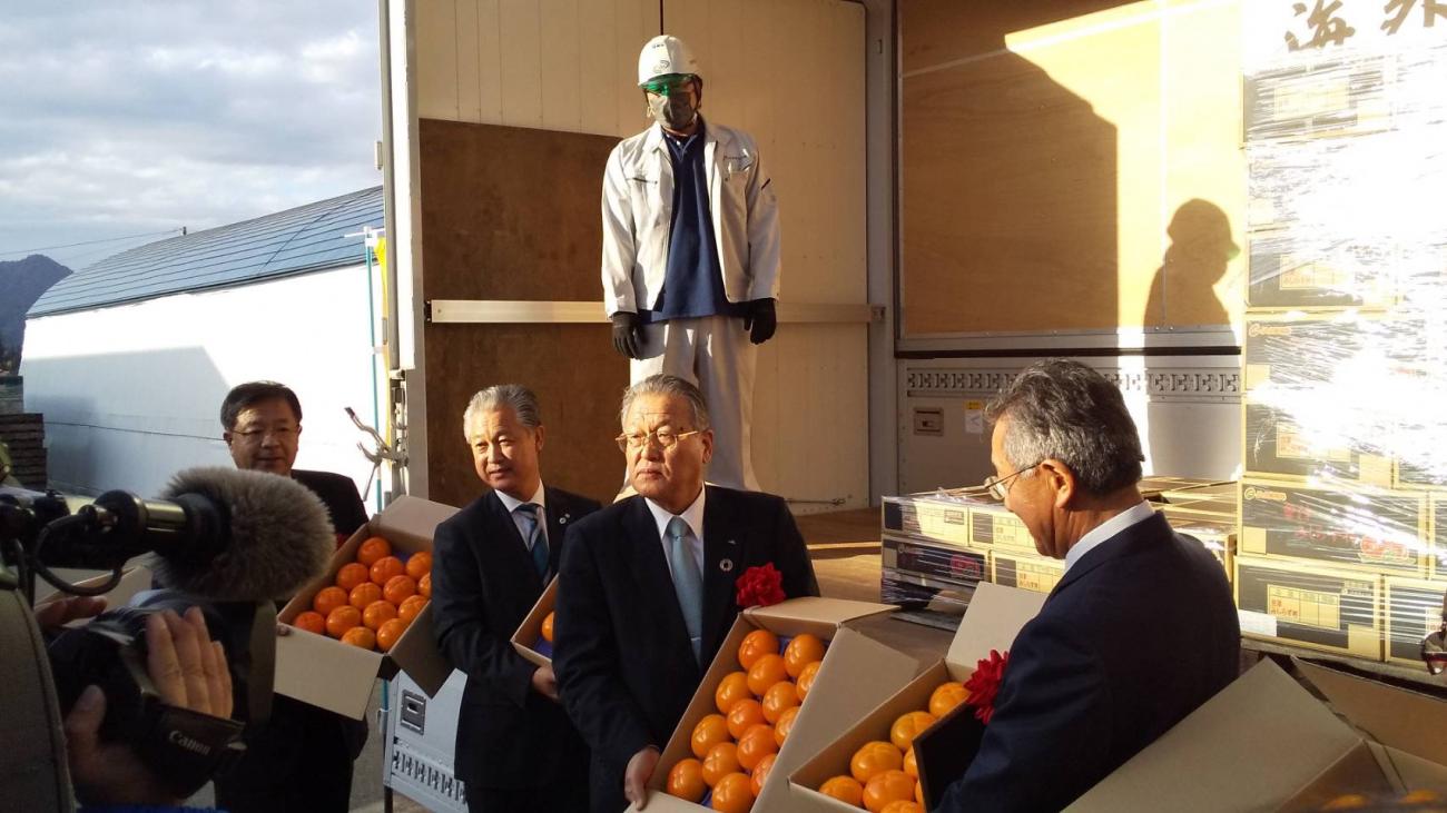 会津みしらず柿海外輸出発送式で、4名のスーツ姿の男性が箱に入ったみかんを持っている様子の写真