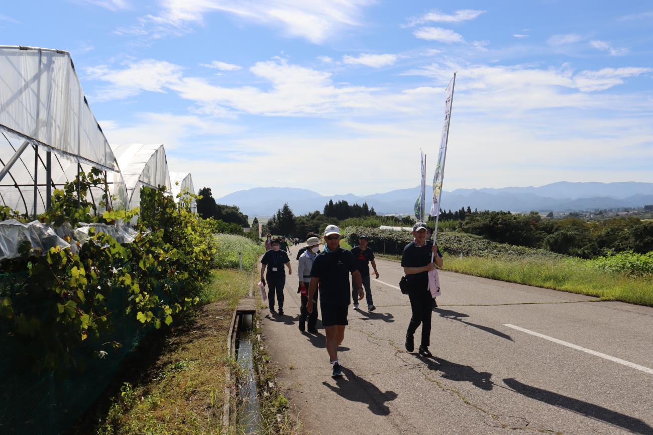 青空の中、参加者の人達と道路を歩きながらふれあいウォーク2022を楽しんでいる町長の写真