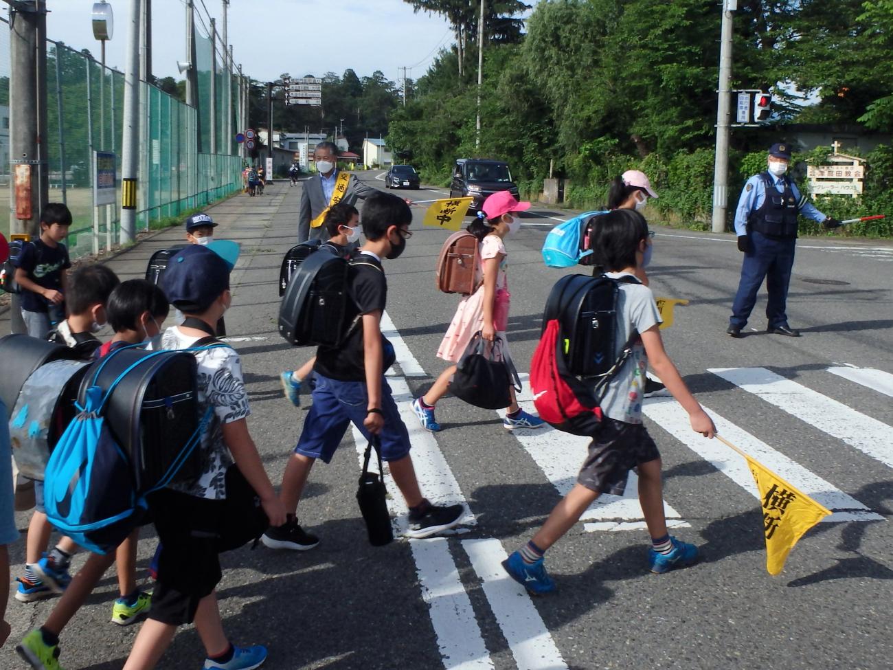 横断歩道を歩く大勢の小学生と、横断を見守る警察官の方と町長の写真