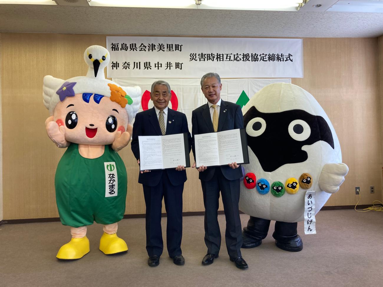 「なかまる」と「あいづじげん」のマスコットキャラクターの間に中井町の町長と並んで記念撮影をしている町長の写真