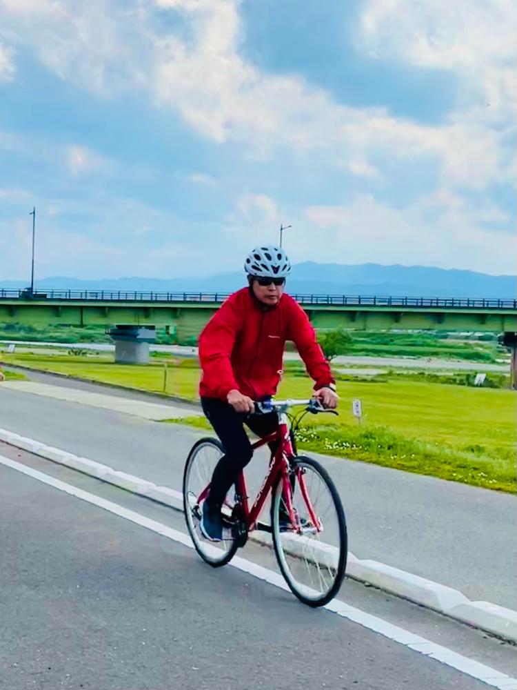白いヘルメットを被りサングラスをかけ赤いウィンドブレーカーを着た町長が、マウンテンバイクに乗って、道路を走っている写真