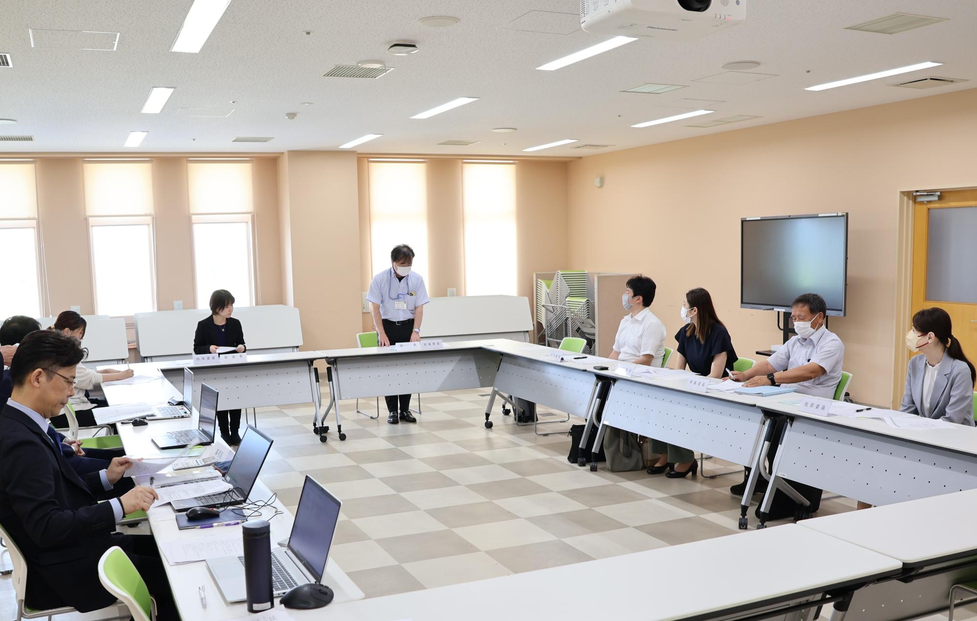 会議室に設置された長テーブルに座って、正面に座っている男性の話を聞いている関係者たちの写真