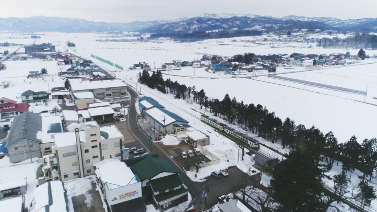 町に雪が積もり電車が走っている様子を上空から写している写真
