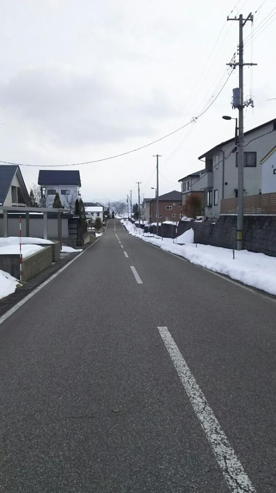 住宅街の間を通っている直線道路があり、脇道にだけ雪が積もっている写真