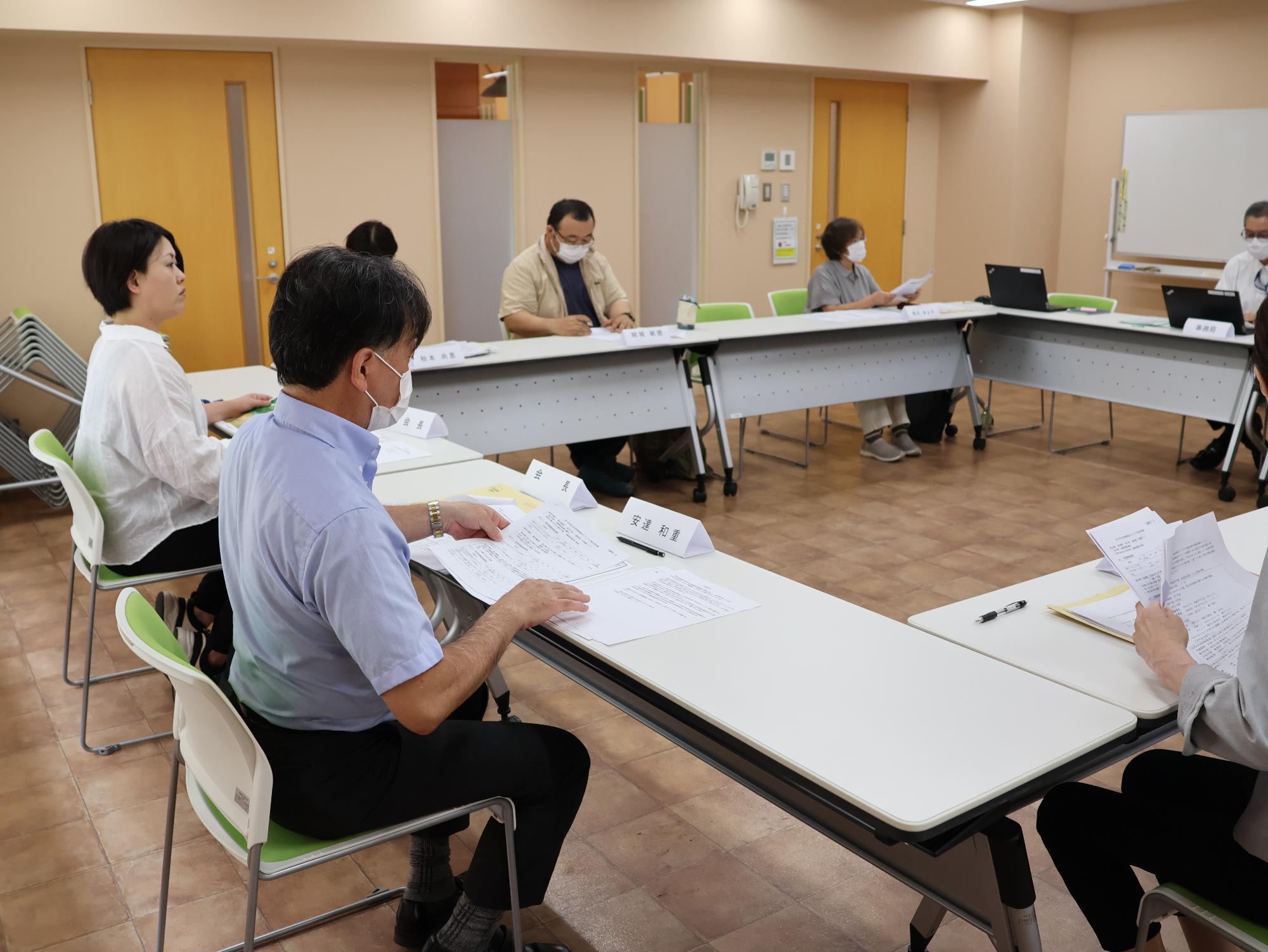 会議室に設置された長テーブルに座って、正面に座っている男性の話を聞いている関係者たちの写真