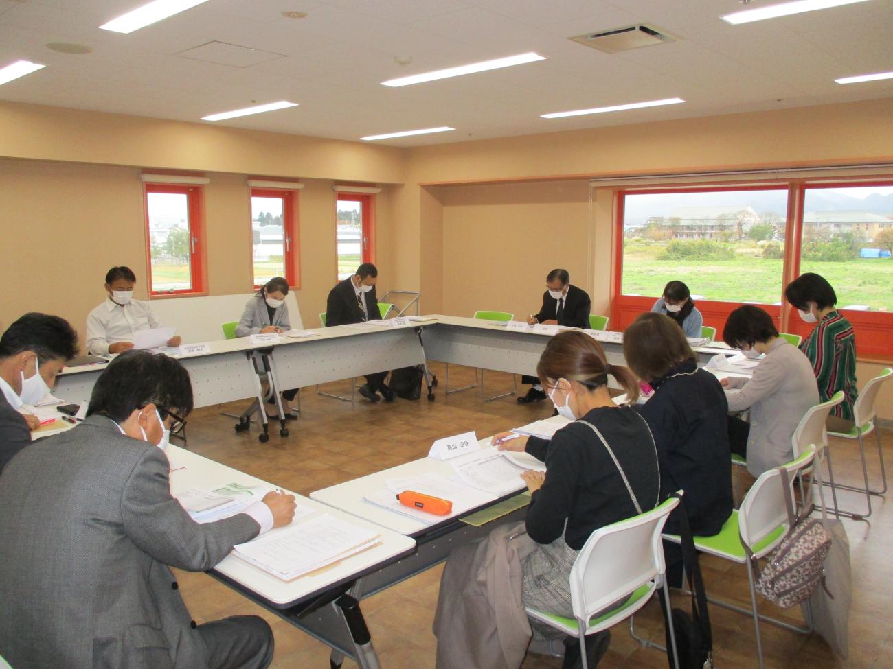 長テーブルがロの字型に設置された会議室で、12人ほどの関係者たちがペンで資料にメモをしている様子の写真