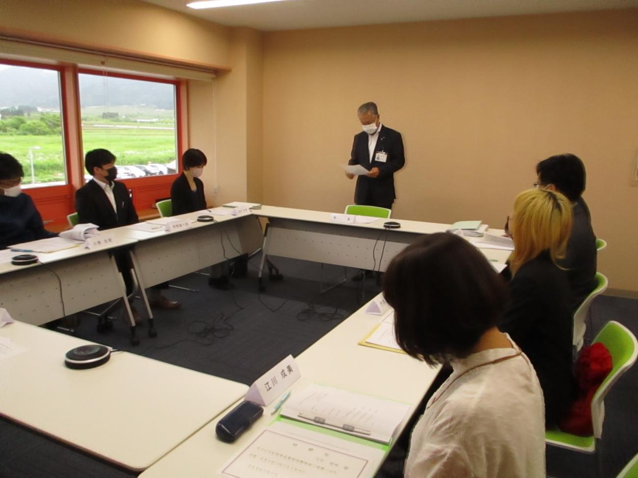 テーブルがロの字型に設置された会議室でスーツ姿の町長が立って話をしている様子と、席に座って話を聞いている関係者たちの写真