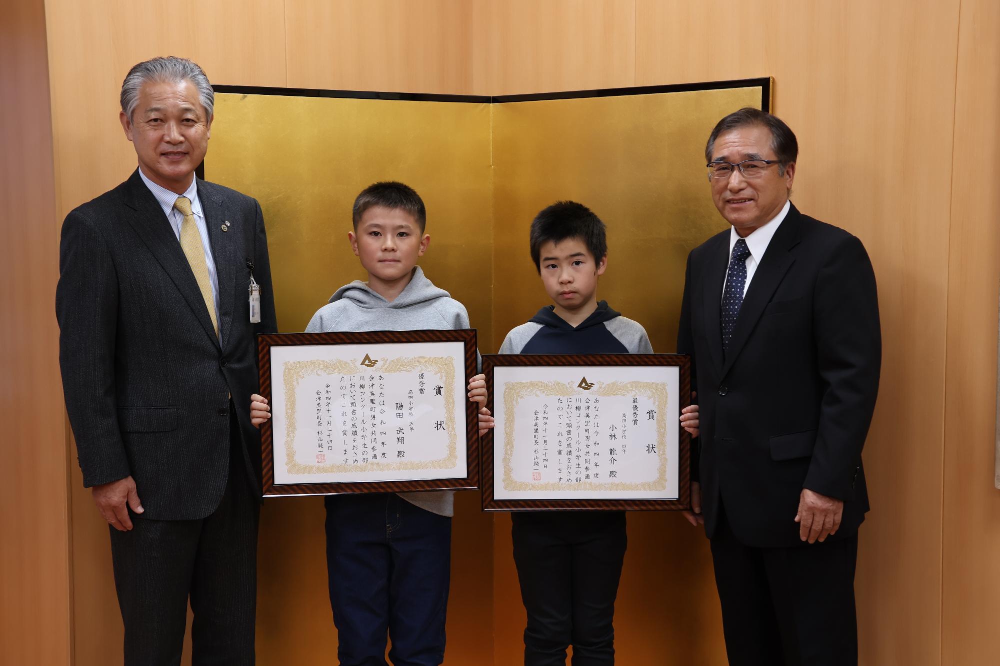 金屏風の前で男子生徒2人がそれぞれ賞状を胸の前に持って立っており、町長と川島忠夫会長に挟まれ記念撮影をしている写真