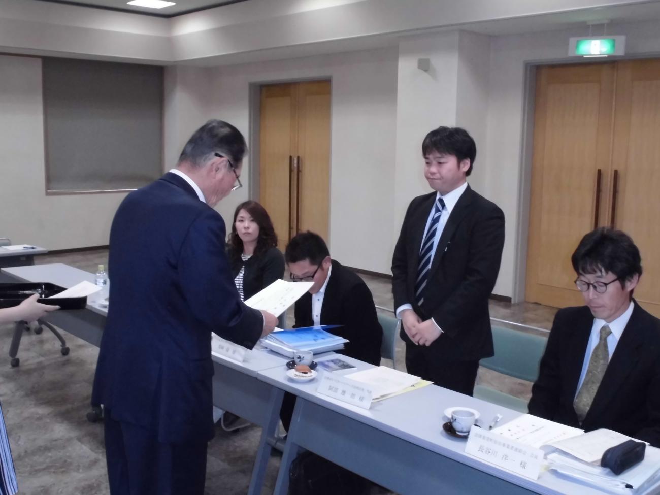 ネイビーのスーツを着た男性（左）が書面を見ながら言い渡しているのを、ストライプのネクタイをした男性（右）が聞いている写真