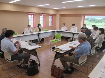 複数の男女が、ロの字型に配置されたテーブルと椅子に座り話をしている協議会の様子の写真
