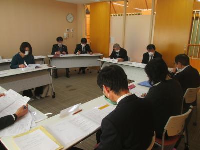複数の男女が、長机と椅子に座り資料を見ながら話をしている協議会の様子の写真