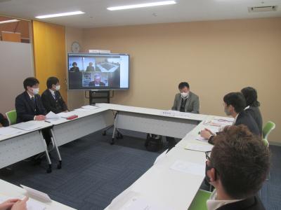 会議室前方のモニターにリモート参加者の顔が映され、ロの字型に配置されたテーブルと椅子に座り話をしている協議会の様子の写真