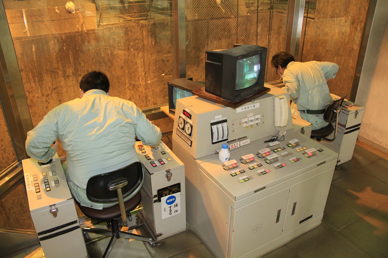 環境センターの管制室で2名の男性がクレーンを操作している様子を後ろから写した写真