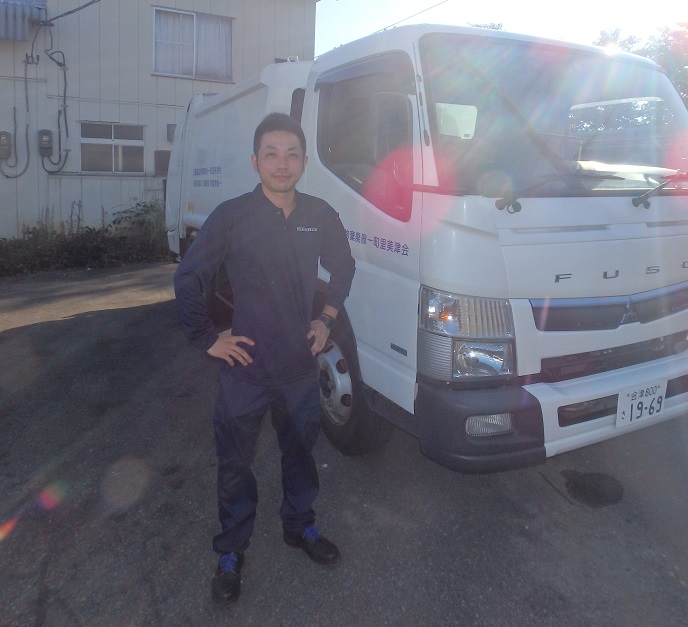 トラックの横で腰に手をあててポーズをとっている組合の鈴木さんの写真