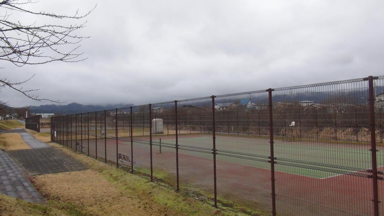 フェンスの奥に見えるテニスコートがある河畔公園庭球場の写真