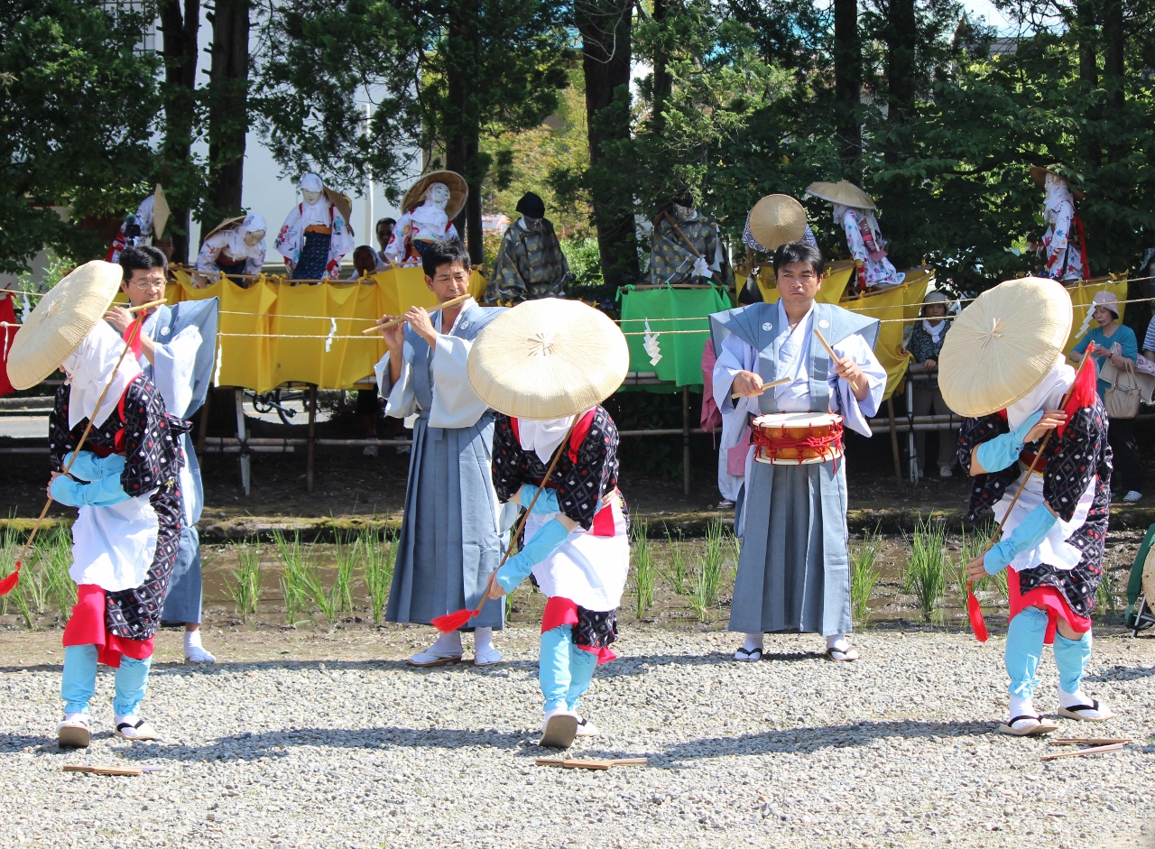 編み笠を被り紺色のひとえの祭り衣装を着て踊る3人と、袴を着て笛と太鼓で音楽を奏でている3人の写真