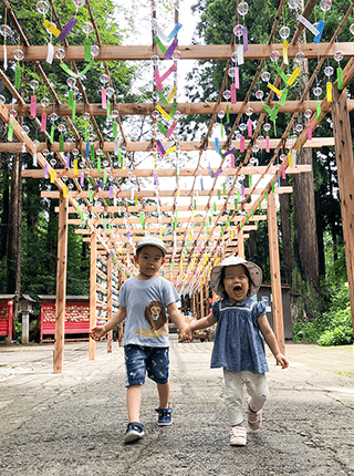 棚に飾り付けられた沢山の風鈴の下を子どもが手をつないで歩いている写真